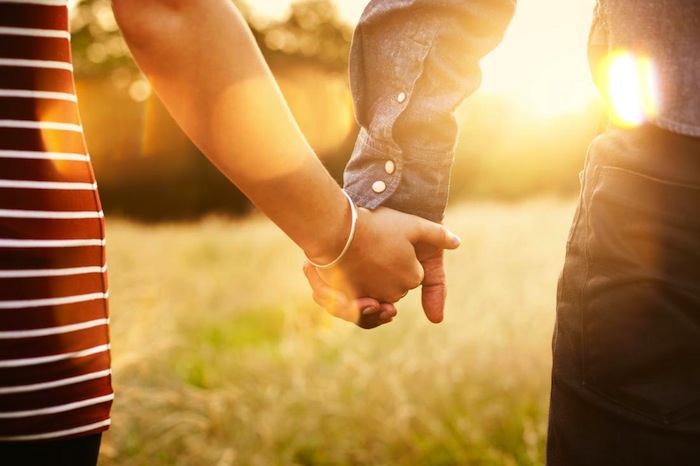 Young couple holding hands with sun-flare.