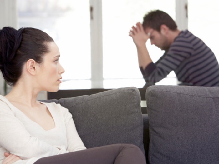 Young woman sitting on sofa, looking at distressed man at table couple fight argue disagreement depressed depression marriage divorce anxiety msnbc stock photo photography